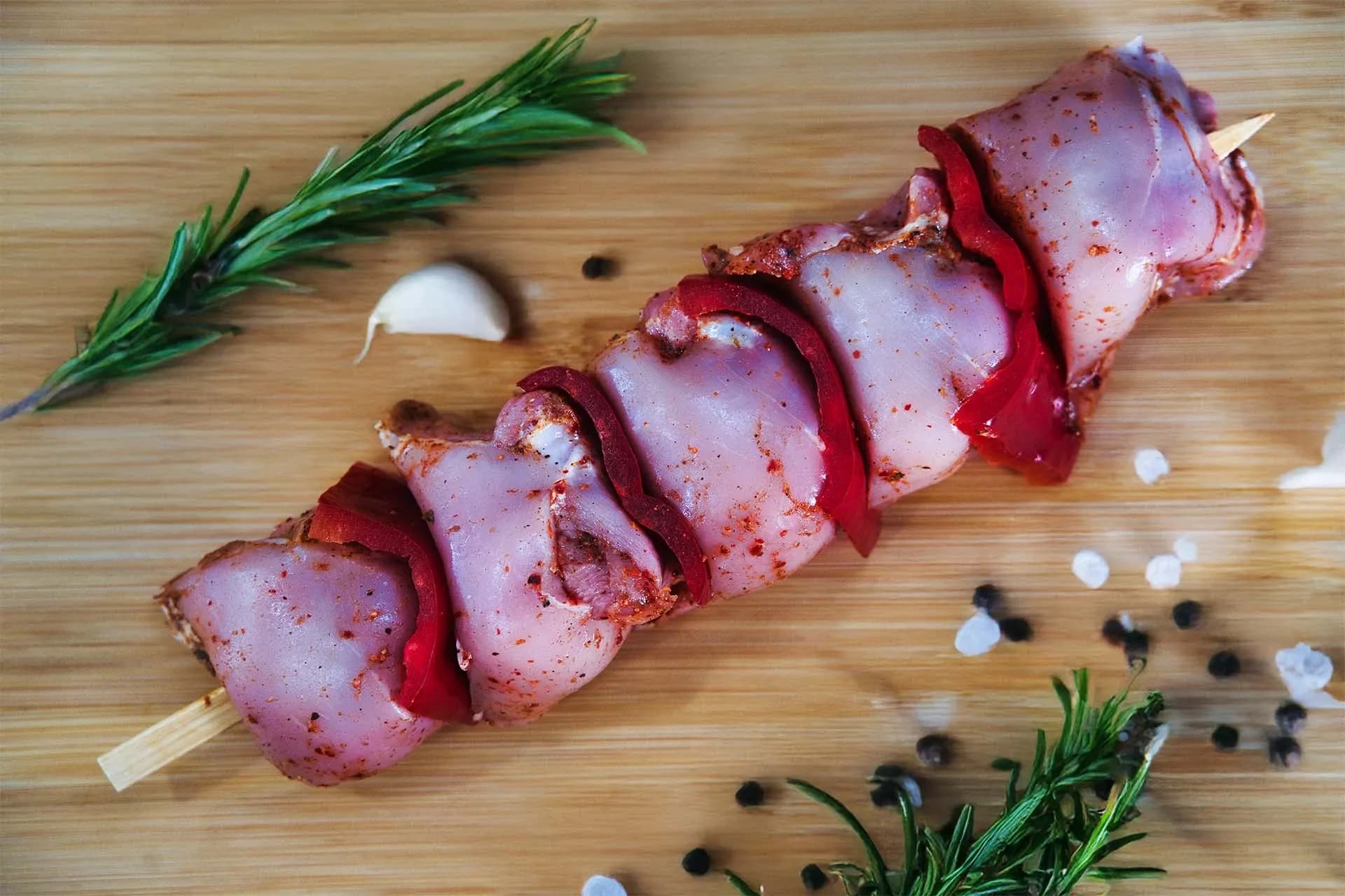 Κοντοσούβλι κοτόπουλο με κομμάτια πιπεριάς σε καλαμάκι, τοποθετημένο σε ξύλο κοπής με δεντρολίβανο, σκόρδο και πιπέρι